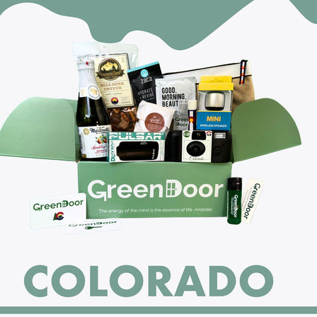 Curated Colorado gift box in green, filled with local snacks, sparkling cider, mini wireless speaker, camera, lip balm and travel pouch.