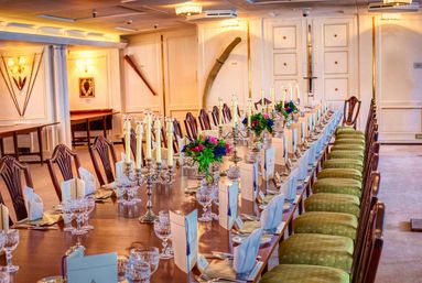 Long elegant banquet table in a classic dining room set for a formal dinner—brass candelabras, crystal glassware, folded napkins, printed menus and colorful floral centerpieces.