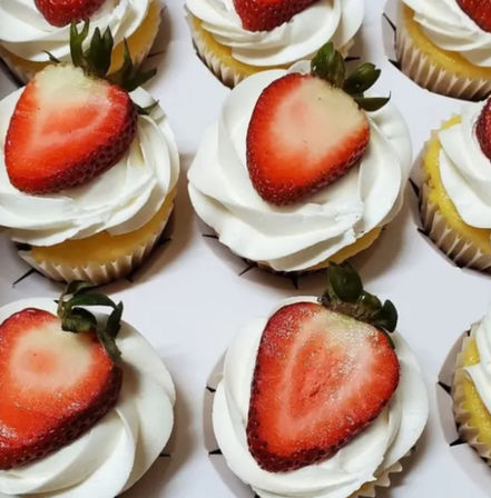 Close-up of vanilla cupcakes with swirled white frosting topped with halved fresh strawberries in a bakery box