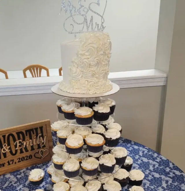 Tiered cupcake tower topped with a white rosette wedding cake and glitter 'Mr & Mrs' topper on a blue lace tablecloth at an indoor reception.