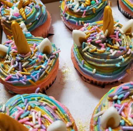 Close-up of pastel rainbow unicorn cupcakes with swirled multicolor frosting, gold edible horns, white fondant ears and rainbow sprinkles