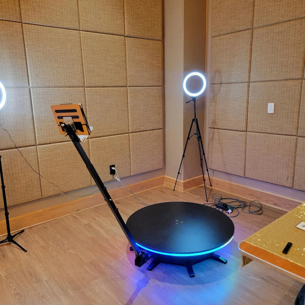 360-degree LED rotating photo booth platform with adjustable tablet mount, illuminated ring lights on tripods and beige acoustic panels in a wood‑floored studio