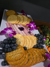 Charcuterie-style appetizer platter with stacked round crackers, rolled deli ham, fresh blueberries and vibrant purple orchid garnishes on a white tray.