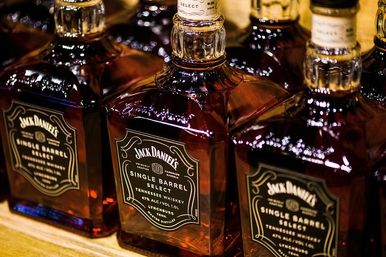 Square glass single-barrel Tennessee whiskey bottles with gleaming dark amber liquid and black labels on a wooden shelf