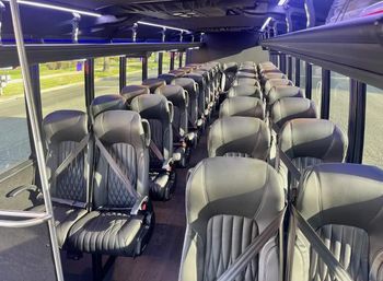 Empty luxury shuttle bus interior with rows of black leather seats with seatbelts, center aisle, overhead luggage racks, LED accent lighting and large windows