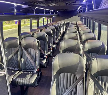 Empty luxury shuttle bus interior with rows of black leather seats with seatbelts, center aisle, overhead luggage racks, LED accent lighting and large windows