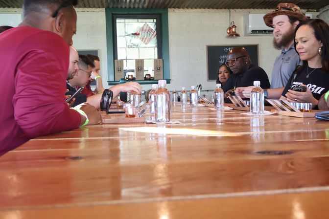 Group gathered around a long wooden tasting bar sampling craft spirit flights and bottled water in a bright distillery tasting room