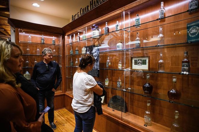 Curious visitors admire vintage whiskey bottles on glass shelves in a warm wood-and-glass distillery museum display