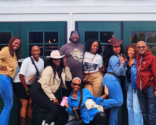 Nine people smiling and posing outside green double doors in Nashville, dressed in casual denim and cowboy hats for a playful group outing.
