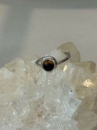 Sterling silver ring with round tiger's eye cabochon set in a serrated bezel, displayed on a clear quartz crystal cluster