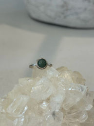 Minimalist silver ring with a round green gemstone resting on a sparkling clear quartz cluster — jewelry product photo.