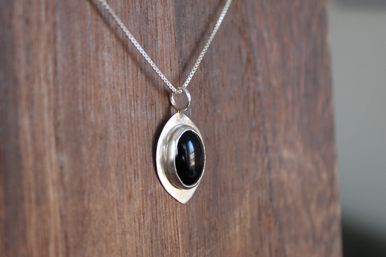 Close-up of a silver pendant necklace with an oval black cabochon stone hanging against a textured wooden background