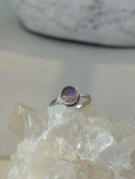 Close-up of a silver ring with a round purple amethyst cabochon perched on a clear quartz crystal cluster — minimalist boho jewelry product shot.