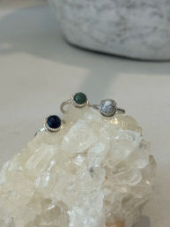 Three silver bezel rings with blue, green, and white marbled stones displayed on a clear quartz crystal cluster on a neutral surface