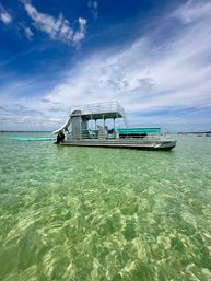 Pontoon boat with upper deck and water slide anchored in shallow crystal-clear turquoise water under a bright blue sky