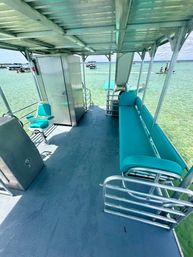 Covered pontoon boat deck with teal bench seating and captain’s chair overlooking clear turquoise shallow water with nearby boats and jet skis.