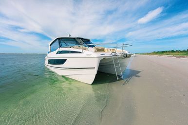 White motor yacht beached in clear shallow turquoise water beside a wide sandy shore, swim ladder down and bright blue sky with wispy clouds.