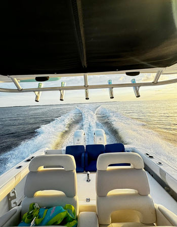 Stern view from an open-deck powerboat with twin outboard engines and T-top rod holders, cutting a golden sunset wake across calm open water.