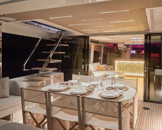 Luxury yacht interior dining area at night with table set for six on teak deck, folding canvas chairs, floating staircase to upper deck, cozy lounge and glowing bar — perfect for sunset dinners.