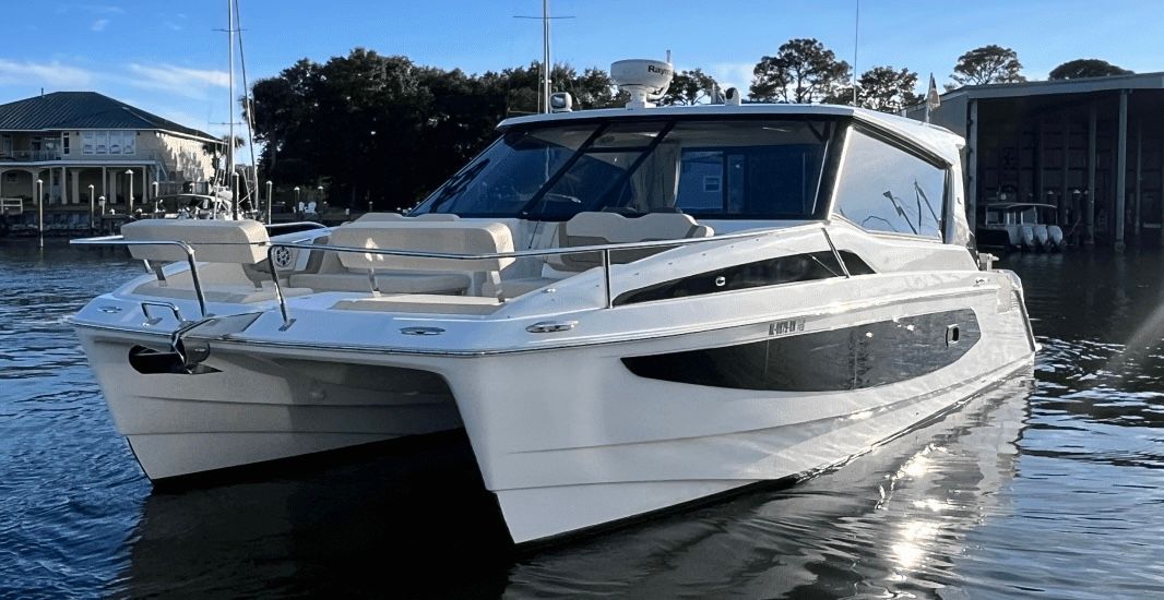 Sleek white luxury catamaran yacht docked at a sunny coastal marina, twin hulls and open deck reflecting on calm water.