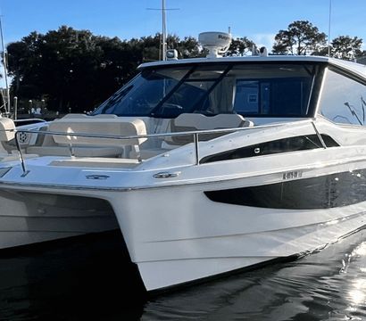 Sleek white luxury catamaran yacht docked at a sunny coastal marina, twin hulls and open deck reflecting on calm water.