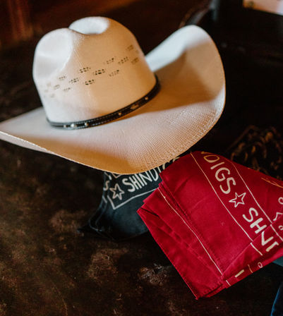 White straw cowboy hat resting on a dark surface beside folded red and black bandanas with western-style star graphics, evoking a country rodeo vibe.