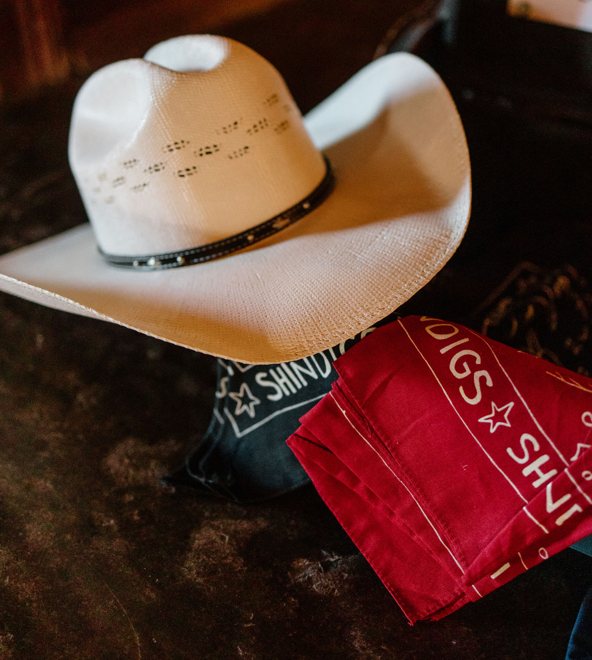 White straw cowboy hat resting on a dark surface beside folded red and black bandanas with western-style star graphics, evoking a country rodeo vibe.