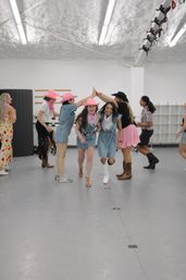 Group of women in denim outfits, pink cowboy hats and boots laughing through a high-five tunnel in a bright indoor dance studio