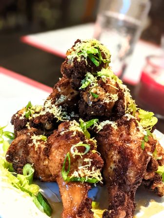 Crispy fried chicken wings piled high, glazed in sticky sauce and topped with grated cheese, sliced scallions and lemon zest on a white plate — a savory restaurant-style appetizer.