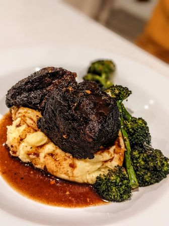 Hearty braised beef short ribs on creamy mashed potatoes with rich brown gravy and roasted broccolini on a white plate
