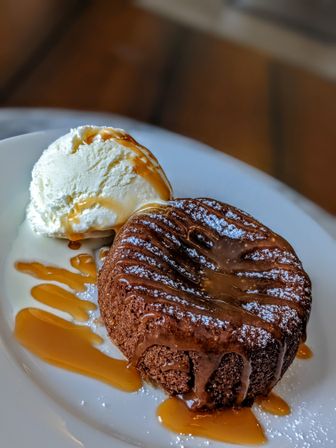 Molten chocolate lava cake dusted with powdered sugar and caramel drizzle, paired with a melting scoop of vanilla ice cream on a white plate — restaurant-style dessert close-up.