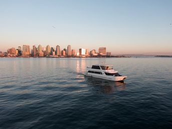 White yacht cruising on calm water at golden hour with San Diego skyline, sunset reflections and the Coronado Bridge in the background