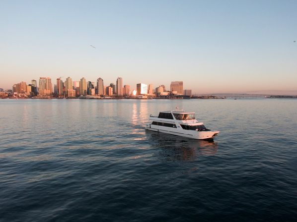 White yacht cruising on calm water at golden hour with San Diego skyline, sunset reflections and the Coronado Bridge in the background