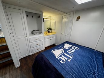 Compact bedroom with white built-in cabinetry and vanity sink, navy nautical blanket on the bed, brass hardware and warm wood-look flooring