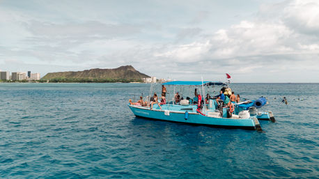 Turquoise snorkel boat with passengers on the Pacific off Waikiki, Oahu, with Diamond Head crater and the Honolulu skyline in the background on a sunny, partly cloudy day.