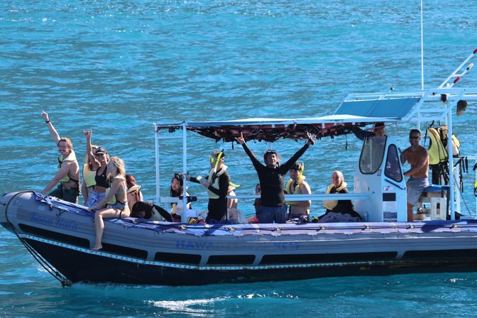 Snorkeling tour on an inflatable boat in turquoise tropical water, passengers in life jackets and snorkel gear smiling and waving under a shaded canopy