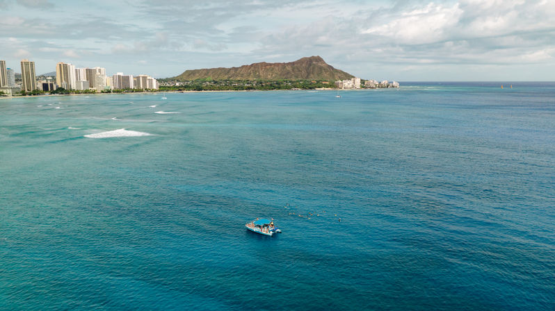 Aerial view of turquoise Pacific with a small tour boat and snorkelers off Waikiki beach, Honolulu skyline and Diamond Head crater in the background