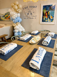 Coastal bachelorette brunch table setting at Isle of Palms, SC with navy placemats, rolled name towels, a cream-and-blue balloon garland and a 'Last Toast' banner.