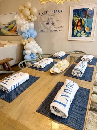 Coastal bachelorette brunch table setting at Isle of Palms, SC with navy placemats, rolled name towels, a cream-and-blue balloon garland and a 'Last Toast' banner.