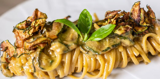 Creamy Italian-style spaghetti twirl with zucchini ribbons, crispy zucchini chips and fresh basil garnish on a white plate