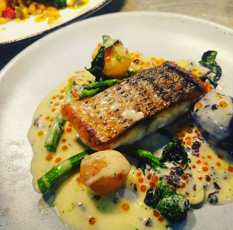 Crispy-skinned seared fish fillet on a creamy sauce with orange fish roe, baby potatoes and broccolini — plated gourmet seafood dish.