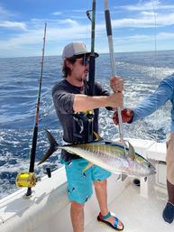 Angler on a fishing boat holding a freshly caught yellowfin tuna over blue open ocean under a sunny sky during a deep-sea fishing trip
