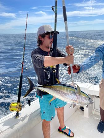 Angler on an offshore sportfishing boat holding a freshly caught yellowfin tuna over the calm blue open ocean under a sunny sky