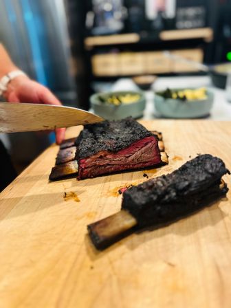 Sliced smoked beef short ribs with blackened bark and pink smoke ring on a wooden cutting board in a kitchen, ready for serving