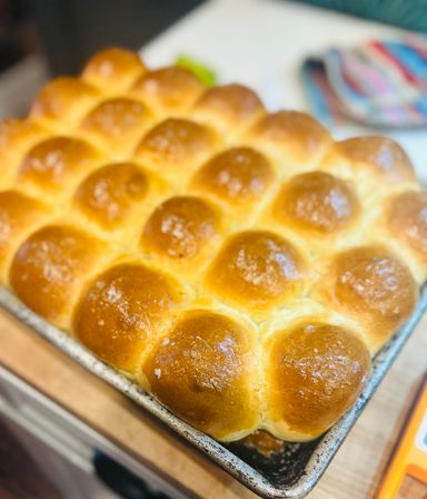 Freshly baked golden dinner rolls — soft, pillowy brioche-style buns nestled in a metal baking pan on a kitchen countertop.