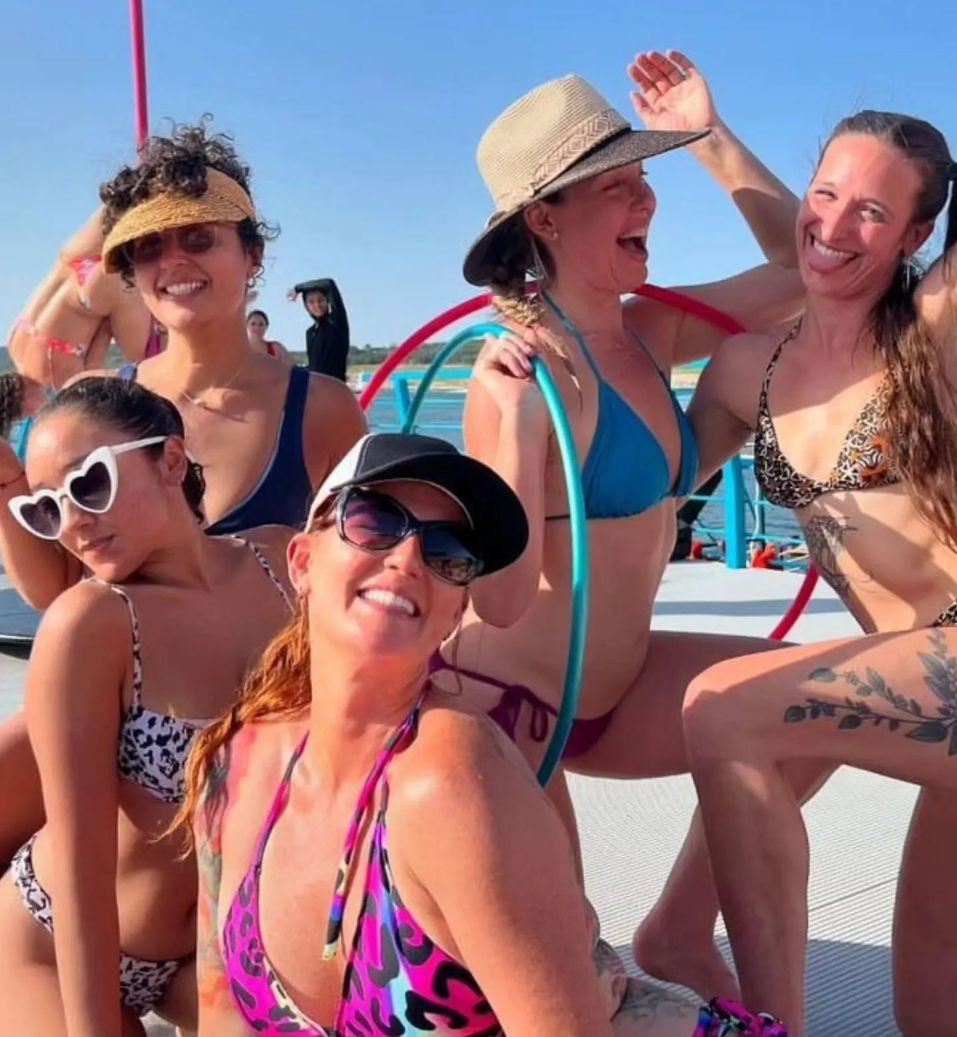Group of smiling women in colorful bikinis, sunglasses and sun hats posing with hula hoops on a sunny boat deck by the blue ocean — playful summer beach vibe.