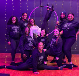 Group of women in matching Austin, TX sweatshirts posing with an aerial hoop (lyra) in a purple-lit fitness studio decorated with string lights