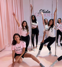 Smiling women striking poses around chrome poles in a pink dance studio, wearing matching 'Last Disco' tees and leggings for a playful bachelorette-style pole fitness class.