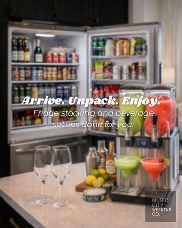 Open refrigerator packed with canned and bottled drinks beside a dual frozen-drink dispenser and cocktail glasses on a kitchen counter — stocked fridge and beverage setup for vacation rentals.