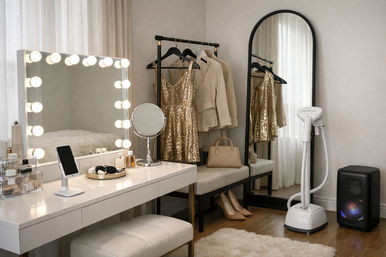 Glam home dressing room with a lighted Hollywood vanity and makeup mirror, gold sequin dress and beige blazer on a clothing rack, arched full-length mirror, garment steamer, nude heels and a small handbag on a bench